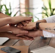 Hands from a diverse team stack on a table symbolizing unity and teamwork in a modern office setting.